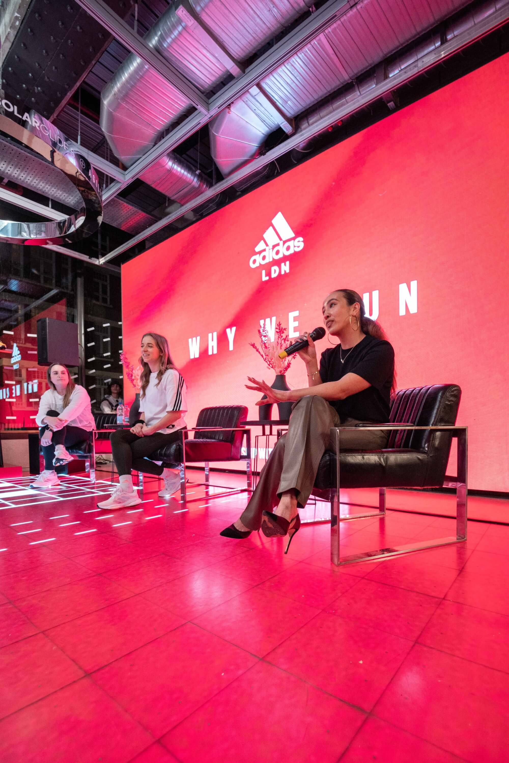 Amira sits on a black chair on stage talking into a microphone at an Adidas London event