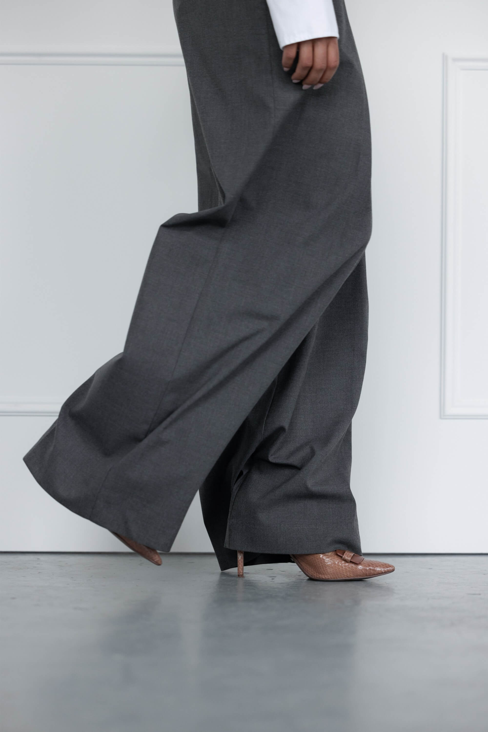 A close up shot of a woman wearing grey tailored suit trousers and pointed pale pink stiletto heels.