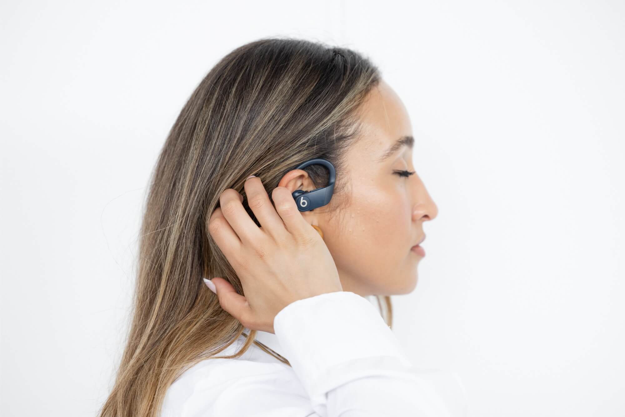 Close up side profile of Amira tucking her hair behind her ear. She wears in-ear Beats headphones.